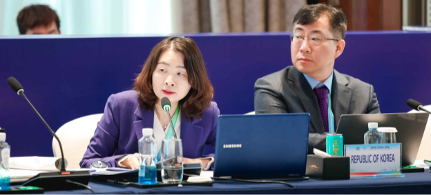 Photo of delegates from the Republic of Korea participating in an international meeting. The image shows two representatives seated at a conference table with laptops and microphones, speaking and taking notes during the session. A nameplate reading “Republic of Korea” is displayed in front of them, indicating national representation at the meeting, while other delegates are seated in the background.